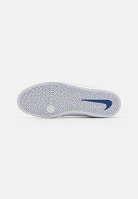 Balts kedu zole ar teksturētu gumijas rakstu, ar zilo Nike swoosh logotipu. Apaļa akcentējoša detaļa centrā, kas paredzēta saķerei.