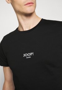 Černé bavlněné tričko s kulatým výstřihem, na levé straně hrudi s bílým logem "JOOP! JEANS". Hladká textura, přiléhavý střih.