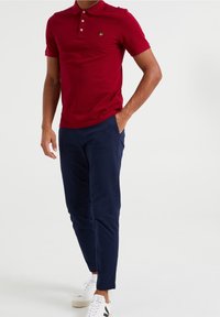 Röd polo t-shirt med krage, korta ärmar och en liten grön logotyp. Matcher med marinblå chinos och vita sneakers. Slät tygkvalitet.