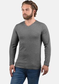 Grijs langarm V-hals shirt gemaakt van zachte stof, met een aansluitend ontwerp en een gladde textuur. Gecombineerd met een blauwe spijkerbroek.