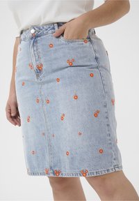 Džínová sukně s světle modrým omakem, s vyšitými oranžovými květy a zelenými listy. Design zahrnuje přední kapsy a zipové zapínání.