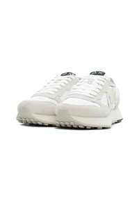 Zapatillas deportivas blancas que combinan gamuza texturizada y cuero liso, con un logotipo negro en la lengüeta y una suela de goma.
