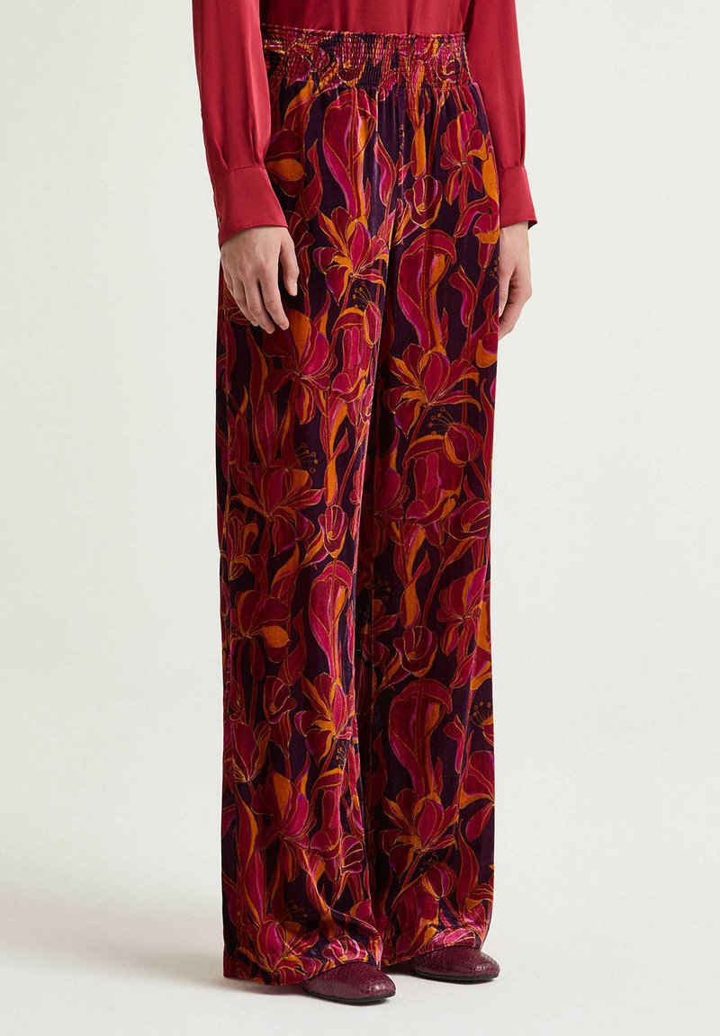 Hose mit weitem Bein und floralem Muster in Rottönen, Orange und Lila. Glatter Stoff mit elastischem Bund, kombiniert mit einem roten Oberteil.