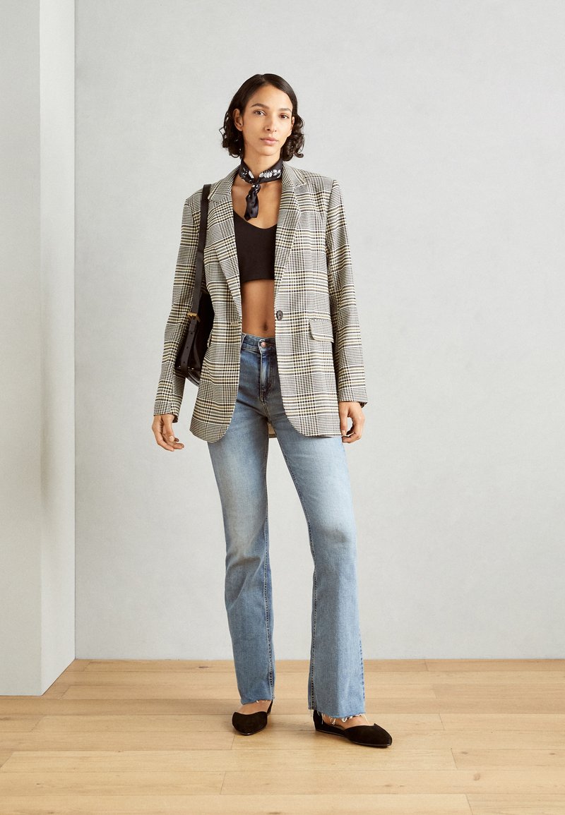 Kraciasty blezer z pojedynczym guzikiem, zestawiony z krótką czarną bluzką i jasnoniebieskimi dżinsami w fasonie dzwonów. Dodatki to czarna torba i szalik.