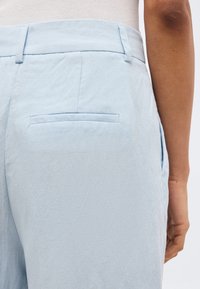 Φωτεινό γαλάζιο παντελόνι ραμμένο με πλάγια τσέπη στην πλάτη, φορεμένο με λευκή ριμπ μπλούζα, με ορατό μέρος του δεξιού μπράτσου και του χεριού.