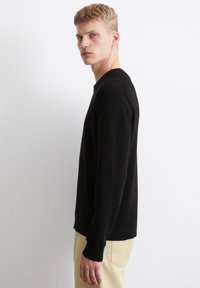 Schwarzer Strickpullover mit langen Ärmeln und gerippter Textur. Verfügt über einen runden Halsausschnitt und einen geraden Schnitt. Wird mit beigen Hosen getragen.