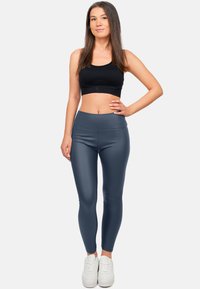 Hoge taille, nauwsluitende legging in een donkergrijze stof, met een gladde textuur en minimale stiksels, gecombineerd met witte sneakers.
