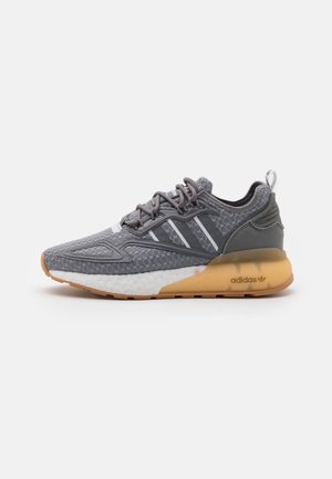 Szary sneaker Adidas z białą śródpodeszwą, gumową podeszwą zewnętrzną, trzema białymi paskami po bokach i sznurowanym zapięciem na białym tle.