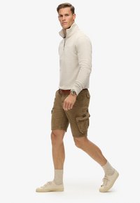 Pull beige avec zip, shorts cargo marron avec poches, baskets beiges et chaussettes gris clair. Tenue décontractée au design fonctionnel.
