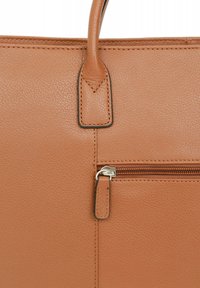 Tan leren handtas met zichtbare gestructureerde nerf. Kenmerken zijn een handvat aan de bovenkant en een ritsvak aan de voorkant met zilverkleurige hardware.