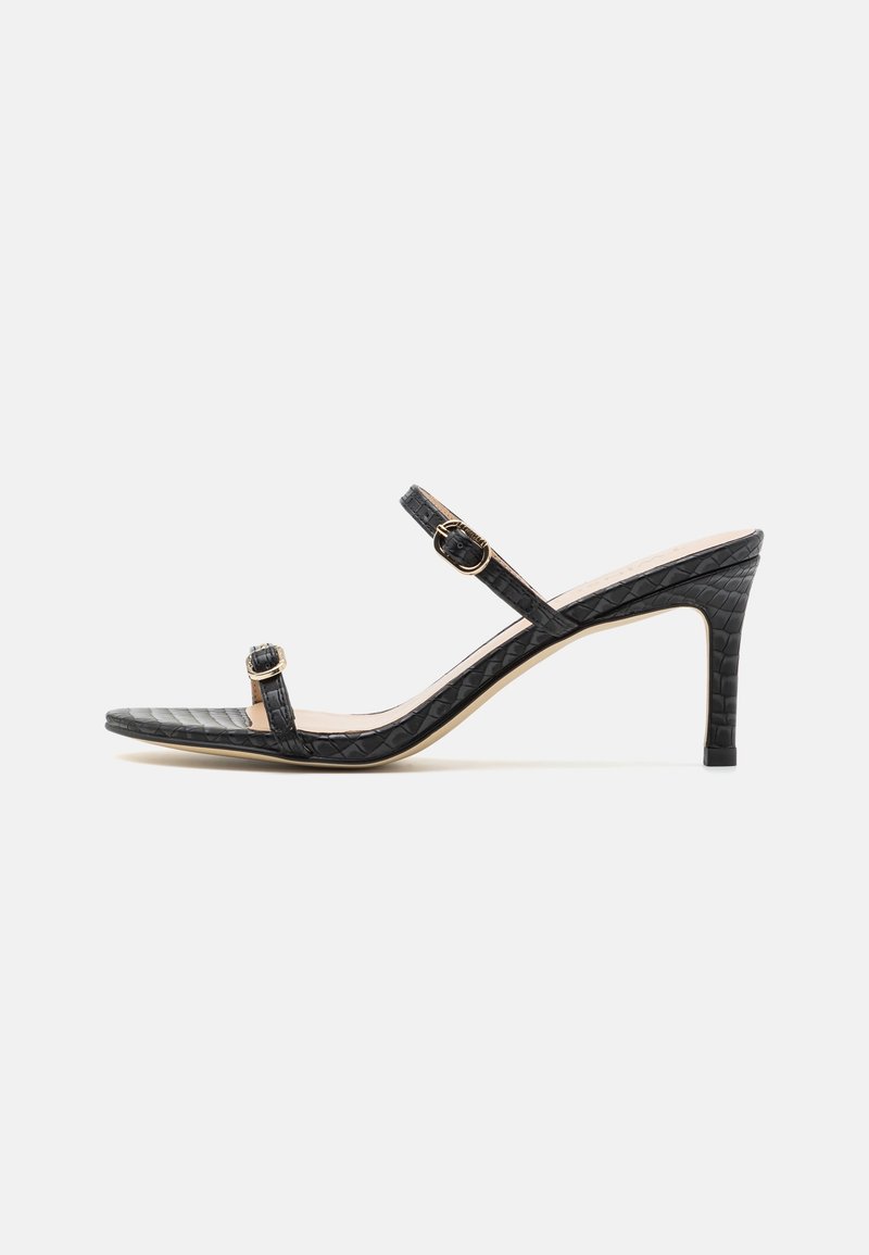 Sandales à talons noires avec une texture crocodile, bout ouvert, brides de cheville et quincaillerie dorée. Talon aiguille de hauteur moyenne.
