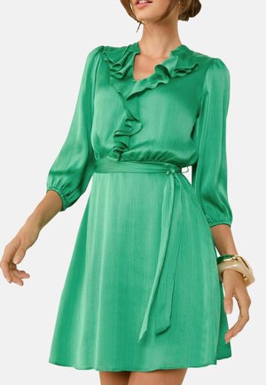 Groene satijnen jurk met een gerimpelde halslijn en driekwartmouwen. De taille is accentueert met een bijpassende strikceintuur.
