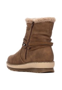 Botas de tobillo de cuero sintético marrón con un suave collarbeige, correas decorativas, cremallera lateral y una suela de goma texturizada.