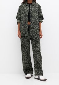 Green leopard print jacket and pants set, made of cotton with a relaxed fit. Features large pockets and a black cropped top underneath.