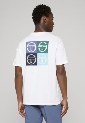 Uomo visto di spalle che indossa una maglietta bianca con quattro loghi quadrati colorati sul retro e pantaloni blu su sfondo uniforme.