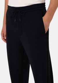 Joggers negros de tela suave con cintura elástica, cierre con cordón, bolsillos laterales y un patrón texturizado a lo largo de los lados.
