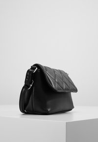 Borsa a mano in pelle nera con un motivo trapuntato sul risvolto e accessori in metallo argentato. Ha un design strutturato e una tracolla removibile.