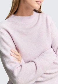 Pulover tricotat de culoare mov deschis, cu decolteu înalt, mâneci lungi și o textură moale. Manșetele și tivul sunt ușor dantelate pentru detaliu.