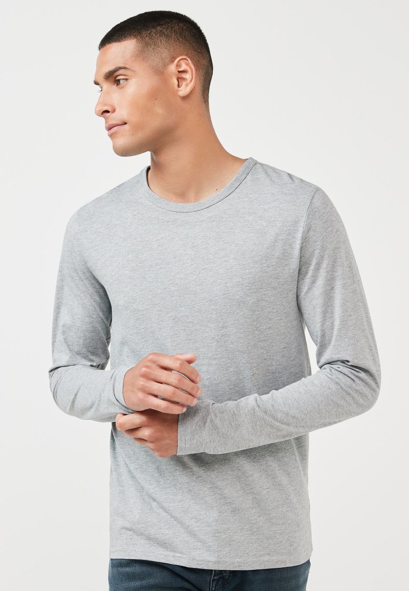 Grå langærmet t-shirt lavet af blødt bomuld. Har en rund halsudskæring og en subtil tekstur, båret med mørke jeans.