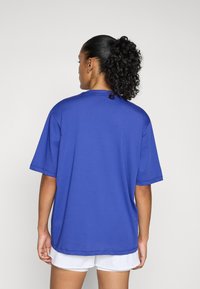 Kék rövid ujjú póló, kerek nyakkivágással és egyenes szabással. Simább anyagból készült, látható varrási részletekkel.