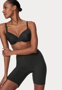 Sujetador negro sin costuras con copas moldeadas y tirantes ajustables, combinado con pantalones cortos moldeadores negros de cintura alta. Textura suave y diseño ajustado.