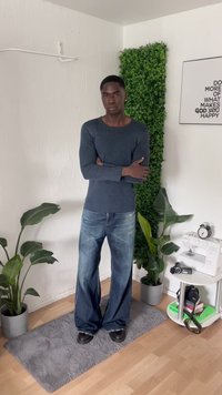 Blue ribbed long-sleeve shirt with a round neckline, paired with wide-leg faded jeans and black shoes. Surrounded by green plants.