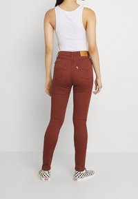 Jeans ajustados de color óxido con una cintura alta, que cuentan con bolsillos traseros y una etiqueta de cuero con marca. Combinados con zapatillas de cuadros en blanco y negro.