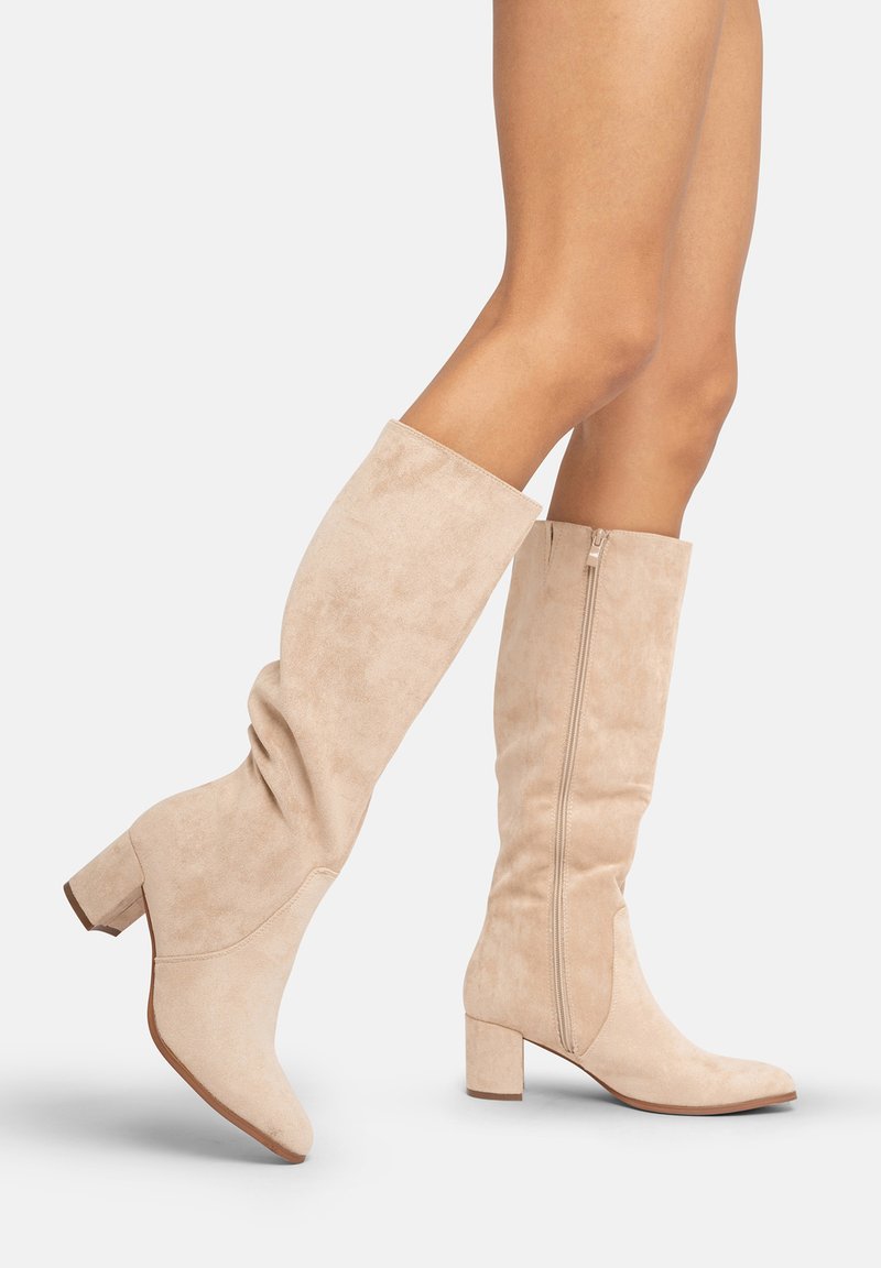 Botas de ante beige hasta la rodilla con tacón bloque, que presentan una silueta curvada y una cremallera lateral para un fácil uso. Textura suave y diseño ajustado.