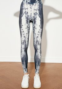 Leggings taille haute avec un motif abstrait bleu et blanc, fabriqués à partir d'un tissu extensible, associés à des chaussures de sport blanches.
