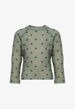 Chemise beige à manches longues avec des motifs en forme de trèfle vert foncé répartis uniformément sur le tissu, avec des coutures visibles aux épaules et à l'ourlet.
