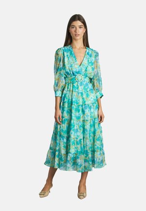 Un vestido largo y en capas en tonos de azul verdoso y aqua con un sutil efecto acuarelado. Presenta mangas abullonadas y un cinturón a juego con una hebilla redonda.