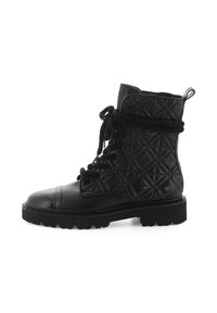 Bottines en cuir noir avec un extérieur matelassé, bout rond, semelle plate et lacets épais. Présente une languette en boucle au niveau du talon.