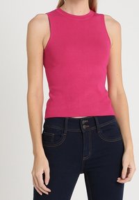 Top ajustado sin mangas de tejido de punto acanalado en un vibrante color rosa. Combinado con unos jeans de mezclilla oscuros que presentan costuras en contraste y una cinturilla con botón.