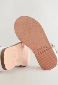 Weiße Sandalen mit einer strukturierten rosa Sohle, die ein Einhorn-Design und Sterne aufweisen, beschriftet mit 'NEXT'. Die Sohle hat einen zweifarbigen braunen Akzent.