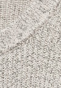 Close-up van beige gebreide stof met ribbels en textuursteken, waarbij de gedetailleerde garenstrengen en de weefstructuur worden getoond.