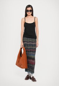 Top din bumbac texturat negru, fustă maxi plisată cu dungi multicolore, geantă tote din suede maro și pantofi slip-on maro. Ochelarii de soare închiși la culoare completează ținuta.