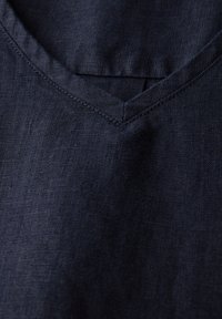 Granatowa lniana bluzka z dekoltem w kształcie litery V, gładką fakturą i subtelnymi detalami w szwie. Materiał wydaje się lekki z lekko stłumionym połyskiem.