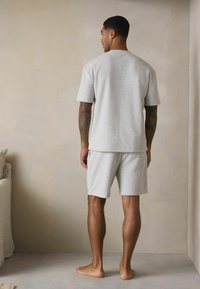 Hellgraues Baumwoll-T-Shirt mit kurzen Ärmeln und passenden Shorts in lockerer Passform, mit sichtbaren Nähten und weicher Textur.