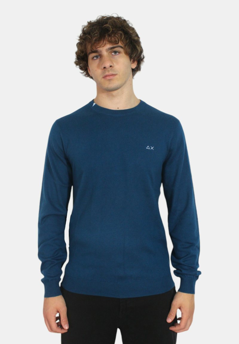 Maglione blu a maniche lunghe realizzato in tessuto morbido, con scollo rotondo e un piccolo logo sul lato sinistro del petto. Texture liscia, design aderente.