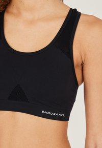 Svart sport-bh med rund halsringning, meshdetaljer och band med "ENDURANCE"-logotyp längst ned. Mjuk, töjbar tyg.