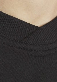 Svart t-shirt med ribbad krage, som visar en närbild av tyget och sömnadsdetaljer, och framhäver dess släta och tajta passform.