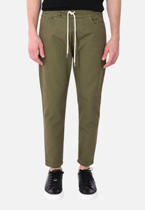 Pantaloni a sigaretta verde oliva con vita elastica regolabile, tasche frontali e dettagli leggermente consumati, abbinati a sneaker nere.
