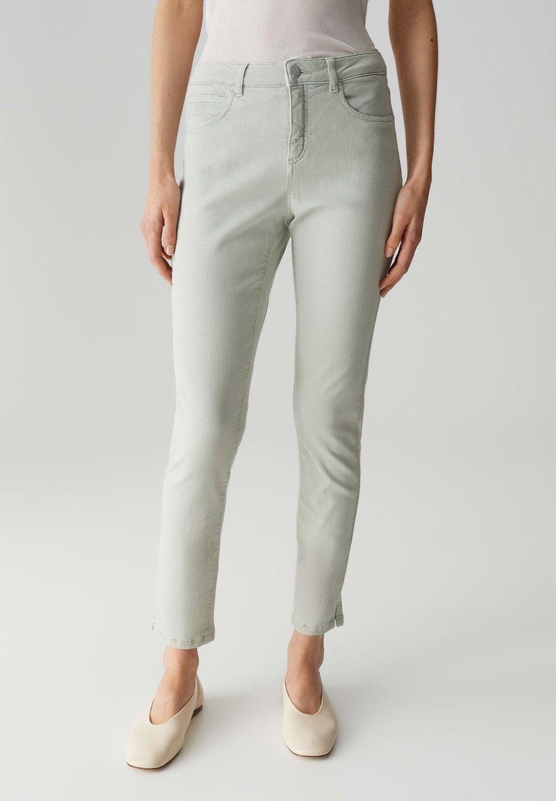 Jeans verde chiaro con una vestibilità slim, design a cinque tasche e dettagli di cucitura sottili. Indossati con scarpe beige chiuse.
