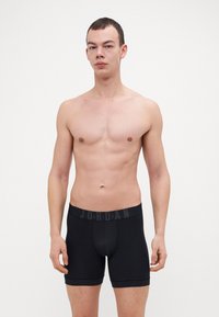 Boxerii negri, cu un design ajustat, cu un bandă elastică cu logo și țesătură netedă, afișați pe un model fără cămașă.