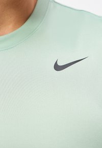 Κοντινή όψη ανοιχτοπράσινου T-shirt της Nike με μαύρο λογότυπο Swoosh στο πάνω μέρος του στήθους κοντά στον λαιμό.