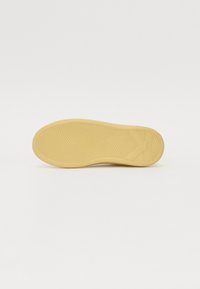 Gummisohle in hellbrauner Farbe mit Wellenmustern für besseren Halt und einer strukturierten Oberfläche. Niedriges Profil mit abgerundeten Kanten.