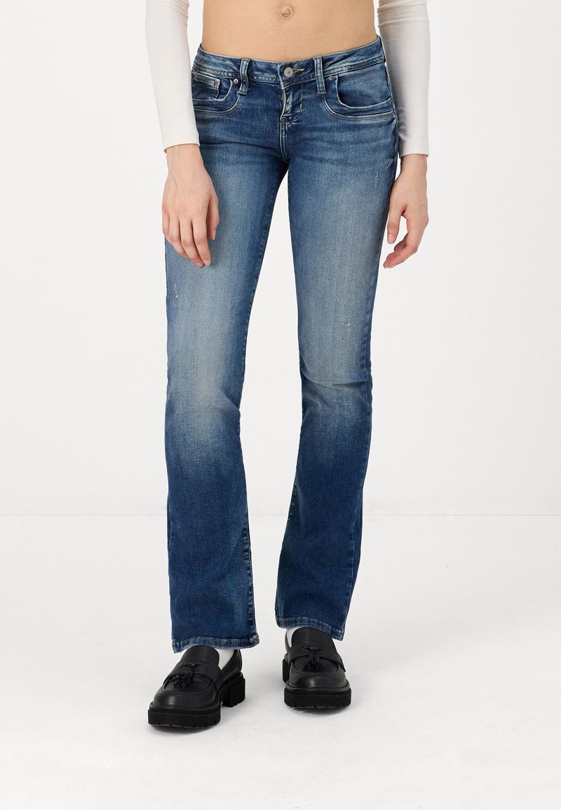 Faded blue denim flared jeans with a mid-rise waist, front pockets, and subtle whiskering detail; paired with black loafers.