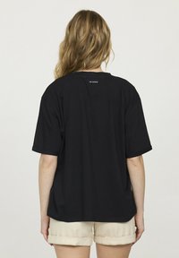 T-shirt noir en coton à manches courtes, à coupe décontractée, avec un petit logo blanc dans le haut du dos. Associé à un short beige clair.