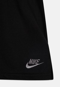 Melnas kokvilnas T-krekls ar mīkstu tekstūru, kuram apakšējā stūrī ir pelēks izšūts Nike logo un apaļa apakšmala.