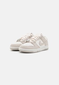 Ljust beige sneakers med texturerad mesh ovandel, slät tådel, snörning och metalliska detaljer. Gummisula med mönstrad slitbana.